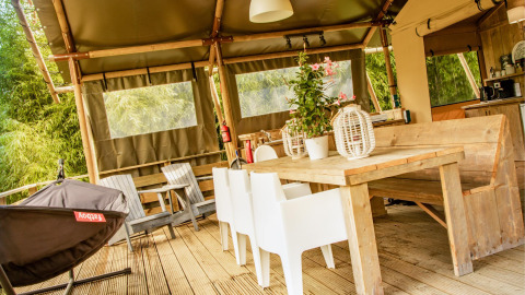 Muebles de madera y sillas blancas en la tienda safari Wood Lodge de Camping Les 3 Cantons, Francia.