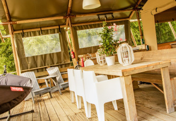Houten tafel en witte stoelen in de Wood Lodge safaritent op Camping Les 3 Cantons, Frankrijk.