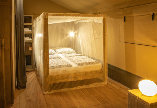 Slaapkamer in de Wood Lodge safaritent op Camping Les 3 Cantons in Frankrijk met muskietennet en houten vloer.