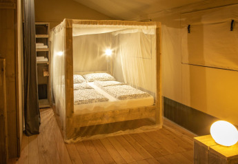 Habitación en la tienda safari Wood Lodge en Camping Les 3 Cantons, Francia, con mosquitera y suelo de madera.