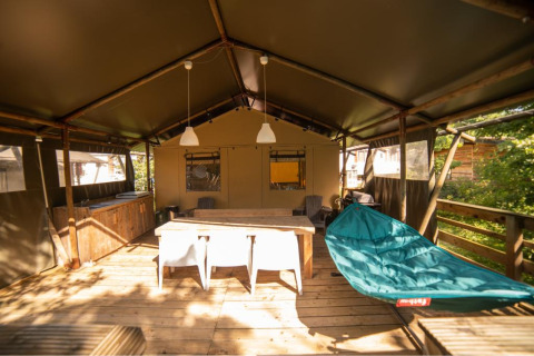 Safari-Zelt Wood Lodge auf Camping Les 3 Cantons in Frankreich, mit Holzterrasse, Hängematte und Esstisch.