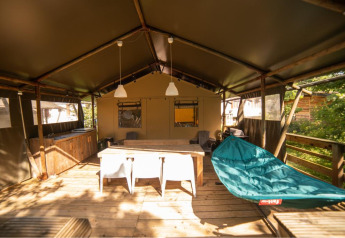 Safari-Zelt Wood Lodge auf Camping Les 3 Cantons in Frankreich, mit Holzterrasse, Hängematte und Esstisch.
