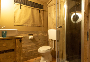 Baño en la tienda safari Wood Lodge en Camping Les 3 Cantons, Francia, con ducha y decoración de madera.