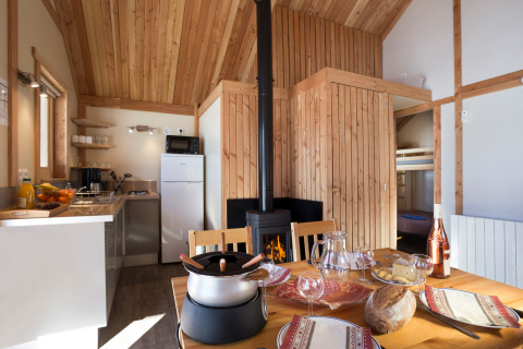 Gemütliche Glamping-Unterkunft mit Holzwänden, gedecktem Tisch, Kamin und moderner Küche im Hintergrund.