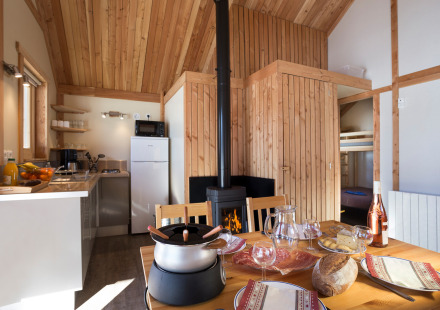 Knusse glamping accommodatie met houten interieur, gedekte eettafel, houtkachel en moderne keuken.