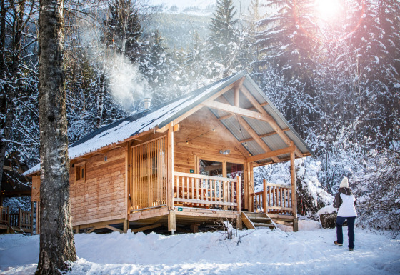 Træhytte dækket af sne i vinterskoven ved Chalet Montana, Les Chalets Huttopia de Bozel, Frankrig.