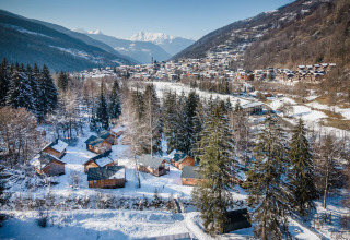 Winter view of Les Chalets Huttopia de Bozel holiday park, snowy cabins in Auvergne-Rhône-Alpes, France.