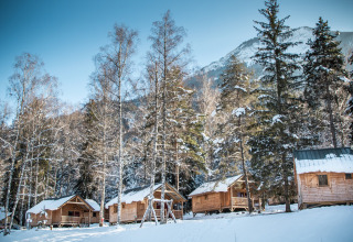 Baite di legno innevate a Les Chalets Huttopia de Bozel, tra alberi e montagne dell'Auvergne-Rhône-Alpes.