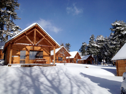 Cabañas de madera cubiertas de nieve en Les Chalets Huttopia de Font-Romeu, rodeadas de pinos en Occitania.