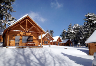 Snow-covered wooden cabins at Les Chalets Huttopia de Font-Romeu holiday park, surrounded by pines in Occitanie.