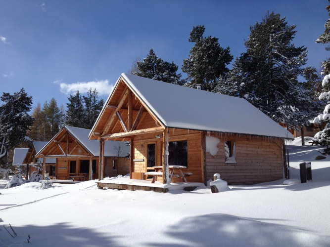 Met sneeuw bedekte houten chalets bij Les Chalets Huttopia de Font-Romeu in het bos van Occitanië, Frankrijk.