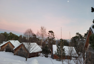 Chalets de bois sous la neige à Huttopia Font-Romeu, Occitanie, France, au coucher du soleil hivernal.