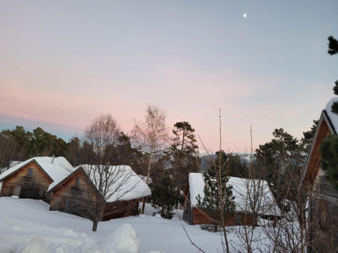 Snow-covered wooden chalets at Les Chalets Huttopia de Font-Romeu in Occitanie, France, at dusk.