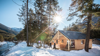 Holzhütte an einem Fluss im Schnee mit Sonnenschein und Bergen, aufgenommen an einer Lodge.