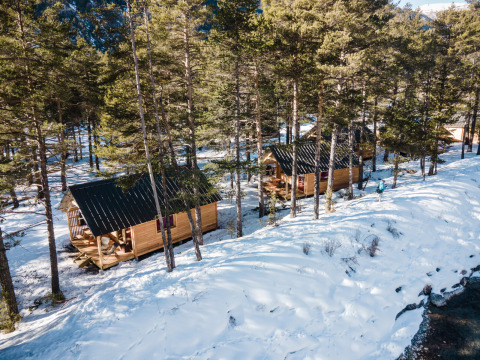 Dos cabañas de madera en un bosque nevado junto a un río en Huttopia la Clarée, Provenza-Alpes-Costa Azul, Francia.