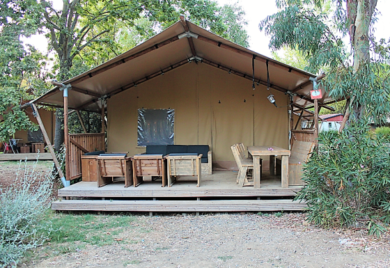 Tenda safari con arredi in legno sulla veranda, circondata da alberi, ideale per rilassarsi all'aperto.