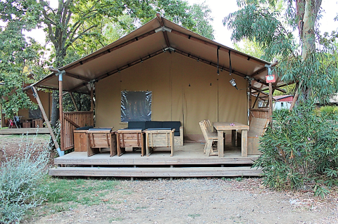 Tenda safari con arredi in legno sulla veranda, circondata da alberi, ideale per rilassarsi all'aperto.