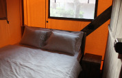 Interior de dormitorio en una tienda safari con cama doble, almohadas y sábanas suaves junto a una ventana.
