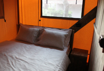 Interior de dormitorio en una tienda safari con cama doble, almohadas y sábanas suaves junto a una ventana.