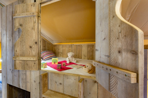 Gemütliches Holzbett mit Kuscheltieren und Spielzeug in einem Safari-Zelt bei Campo dei Fiori, Italien.