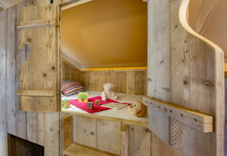 Cozy wooden bunk bed with toys and plush animals inside a safari tent at Campo dei Fiori, Italy.