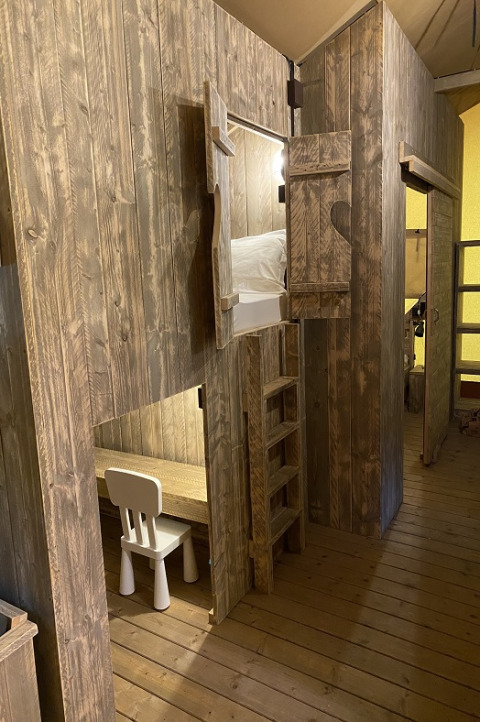 Interni in legno di una tenda safari al Campo dei Fiori con letto a soppalco, scala e scrivania.