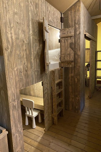 Interior de madera en una tienda safari en Campo dei Fiori con litera, escalera y área de escritorio.