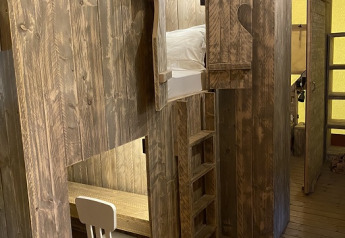 Wooden interior of a safari tent at Campo dei Fiori featuring a loft bed, ladder, and a small desk area.