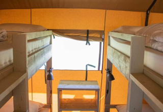 Interior view of Safari tent at Campo dei Fiori, four single beds with rustic wooden frame and warm lighting.