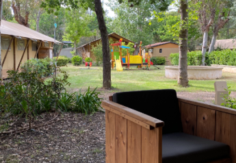 Wooden deck with chair at Safari tent in Campo dei Fiori, Italy, facing playground and lush green trees