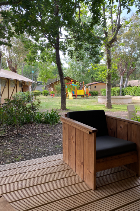 Houten terras met stoel bij Safari-tent in Campo dei Fiori, Italië, uitkijkend op speeltuin en bomen