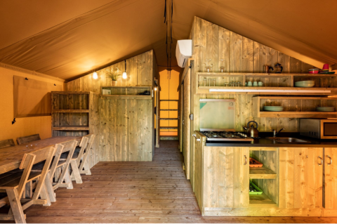 Interior de una tienda safari en Campo dei Fiori (Glamping4all), Italia, con muebles de madera y cocina.