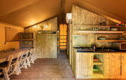 Innenraum eines Safari-Zeltes bei Campo dei Fiori (Glamping4all) in Italien, mit Holzmöbeln und Küche.