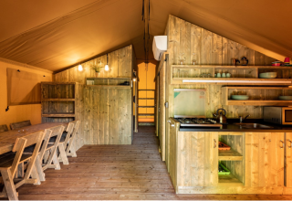 Interior de una tienda safari en Campo dei Fiori (Glamping4all), Italia, con muebles de madera y cocina.