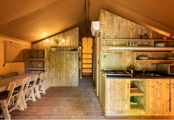 Interior de una tienda safari en Campo dei Fiori (Glamping4all), Italia, con muebles de madera y cocina.