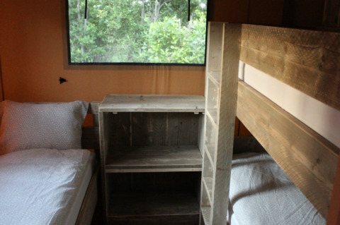 Interior view of safari tent sleeping area with bunk bed, single bed and wood furniture, Campo dei Fiori, Italy.