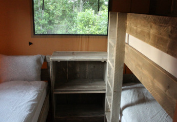 Interior view of safari tent sleeping area with bunk bed, single bed and wood furniture, Campo dei Fiori, Italy.