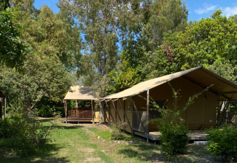 Tente safari au Campo dei Fiori (Glamping4all) en Italie, entourée d’arbres et de verdure lors d’une journée ensoleillée.