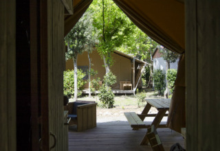 Vista desde el interior de una tienda safari con bancos de madera y vegetación en Campo dei Fiori, Italia.