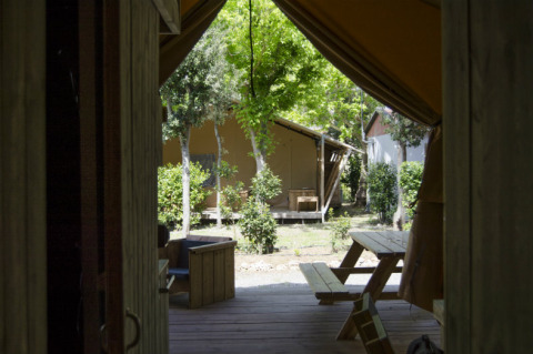 Vista desde el interior de una tienda safari con bancos de madera y vegetación en Campo dei Fiori, Italia.