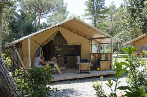 Familia disfruta en la terraza de una tienda safari con cocina y zona de estar, rodeados de naturaleza.