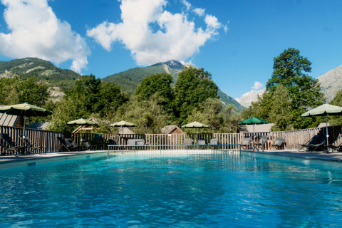 Piscina al aire libre con tumbonas y sombrillas, rodeada de montañas en Huttopia Vallouise, Provenza-Alpes, Francia.