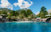 Udendørs swimmingpool med liggestole og parasoller, omgivet af bjerge, i Huttopia Vallouise, Provence-Alpes, Frankrig.