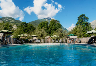 Udendørs swimmingpool med liggestole og parasoller, omgivet af bjerge, i Huttopia Vallouise, Provence-Alpes, Frankrig.
