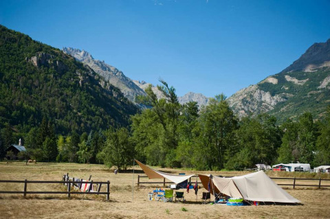 Campamento con tiendas y sillas en un valle montañoso en Huttopia Vallouise, Provence-Alpes-Côte d’Azur, Francia.