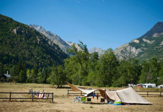 Teltplads med telte og campingstole i grøn dal ved bjerge i Huttopia Vallouise, Provence-Alpes-Côte d’Azur.