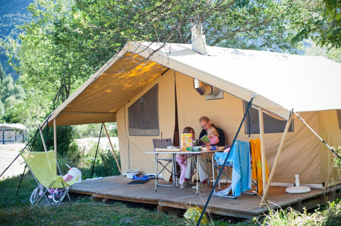 Family relaxing in front of tent with deck at Huttopia Vallouise holiday park, Provence-Alpes-Côte d’Azur, France.