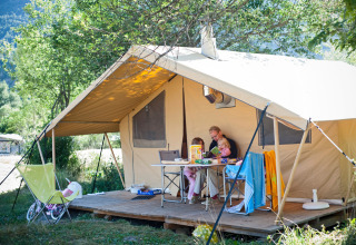 Famille profitant de vacances devant leur tente sur terrasse à Huttopia Vallouise, Provence-Alpes-Côte d’Azur.