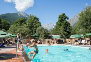 Ferieparkets swimmingpool med gæster, grønne omgivelser og udsigt til bjerge i Provence-Alpes-Côte d’Azur.