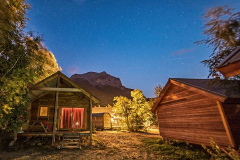 Cabañas de madera iluminadas de noche en Huttopia Vallouise en Provenza-Alpes-Costa Azul bajo un cielo estrellado.